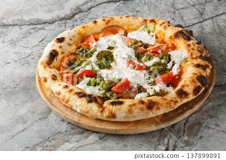 Crispy charred pizza with stracciatella cheese, pesto, ham and tomatoes close-up on a wooden board. Horizontal Crispy charred pizza with stracciatella cheese, pesto, ham and tomatoes close-up on a wooden board. Horizontal 137899891