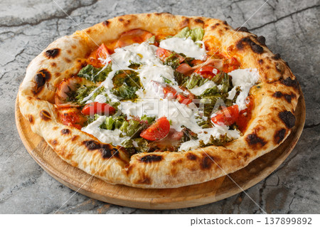 Delicious authentic pizza with stracciatella cheese, pesto, ham and cherry tomatoes close-up on a wooden board. Horizontal Delicious authentic pizza with stracciatella cheese, pesto, ham and cherry tomatoes close-up on a wooden board. Horizontal 137899892