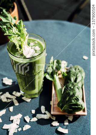 A healthy green smoothie made with fresh celery , standing on a table with a turquoise tablecloth. 137900504