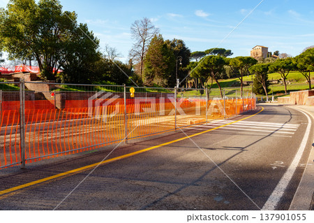 Construction site with barriers along a road near historic buildings in a city park Construction site with barriers along a road near historic buildings in a city park 137901055