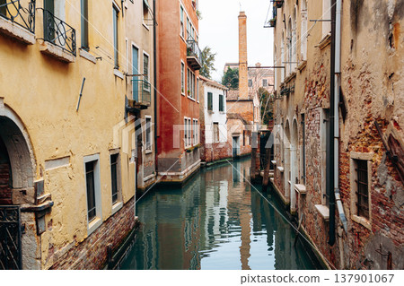 Narrow canal in Venice with buildings on both sides and still water reflecting surroundings 137901067