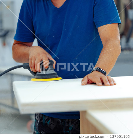Man using an electric sander on wood at a workshop in the afternoon Man using an electric sander on wood at a workshop in the afternoon 137901105