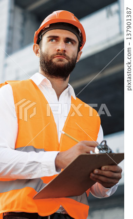 Construction worker looks at plans at a building site during the day 137901387