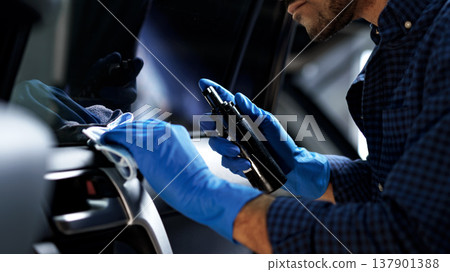 Man cleans car interior while wearing gloves in bright indoor area Man cleans car interior while wearing gloves in bright indoor area 137901388