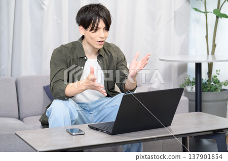 A Japanese man sitting on a sofa and operating a computer. 137901854