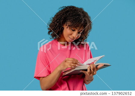 Young african woman reading book with focused smile on blue. Discovery time Young african woman reading book with focused smile on blue. Discovery time 137902652