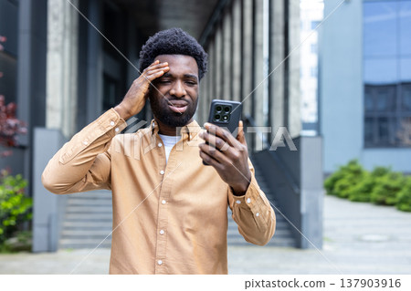 Stressed young person clenching head while looking at a cellphone with a worried expression, reacting to financial problems, business crisis, or upsetting online message Stressed young person clenching head while looking at a cellphone with a worried expression, reacting to financial problems, business crisis, or upsetting online message 137903916