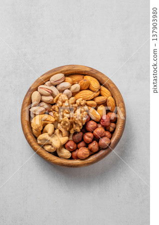 A mix of almonds, cashews, hazelnuts, walnuts, and pistachios in a wooden bowl on a light background. A mix of almonds, cashews, hazelnuts, walnuts, and pistachios in a wooden bowl on a light background. 137903980