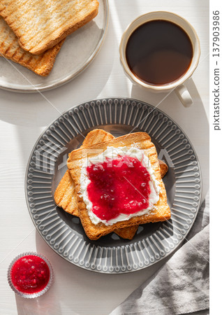 Toast with sweet berry-fruit jam and cream cheese on a plate on a white wooden background with a cup of black coffee Toast with sweet berry-fruit jam and cream cheese on a plate on a white wooden background with a cup of black coffee 137903986