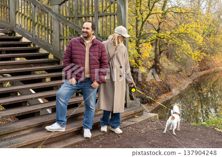 Adult Man And Woman Walking Small Dog Near Wooden Staircase In Autumn Park Adult Man And Woman Walking Small Dog Near Wooden Staircase In Autumn Park 137904248
