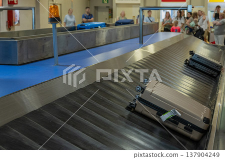 Suitcases On Airport Baggage Claim Conveyor Belt With Travelers In Background 137904249