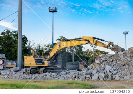 Heavy Excavator Machine Working On Demolition Site With Rubble And Blue Sky Background Heavy Excavator Machine Working On Demolition Site With Rubble And Blue Sky Background 137904250