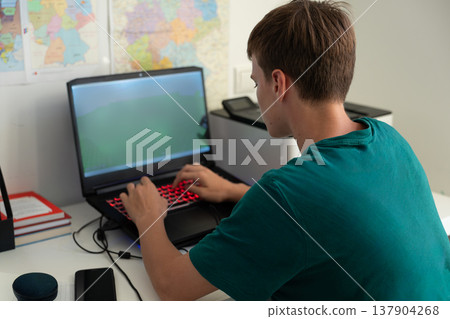 Teenage Boy Using Laptop At Desk In Home Office Interior With Map Background 137904268