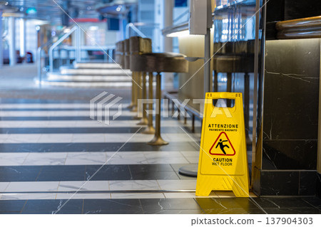 Bright yellow caution sign warning about wet floor placed in a modern indoor environment. Bright yellow caution sign warning about wet floor placed in a modern indoor environment. 137904303