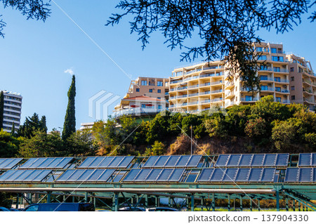 Solar panels and modern apartment buildings on a sunny day. Solar panels under residential buildings on a green hillside. Concept of renewable energy and sustainable architecture. 137904330