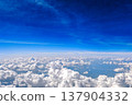 Aerial view of white fluffy clouds in deep blue sky. View from airplane above a sea of white fluffy clouds under rich blue sky. Calm travel cloudscape and freedom concept. 137904332