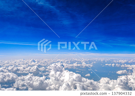 Aerial view of white fluffy clouds in deep blue sky. View from airplane above a sea of white fluffy clouds under rich blue sky. Calm travel cloudscape and freedom concept. Aerial view of white fluffy clouds in deep blue sky. View from airplane above a sea of white fluffy clouds under rich blue sky. Calm travel cloudscape and freedom concept. 137904332