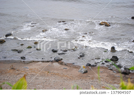 Rocky seacoast of the Sea of Okhotsk on the Kuril Islands in autumn, showing boulders, pebble shores and churning waves under a gray sky. Rocky seacoast of the Sea of Okhotsk on the Kuril Islands in autumn, showing boulders, pebble shores and churning waves under a gray sky. 137904507