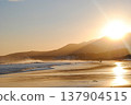 The sandy beach of a Kuril Islands bay glows beautifully at sunset on a sunny day. 137904515