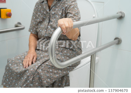 Asian elderly woman use toilet security support rail in bathroom. 137904670