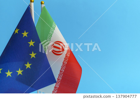 Flags of the European Union and Iran symbols isolated on an empty blue background. Conceptual photography showing international relations and foreign policy discussions between the EU and the Islamic Flags of the European Union and Iran symbols isolated on an empty blue background. Conceptual photography showing international relations and foreign policy discussions between the EU and the Islamic 137904777