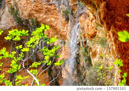 Serene Waterfall Cascading Down Rocky Cliffs Surrounded by Vibrant Green Foliage Serene Waterfall Cascading Down Rocky Cliffs Surrounded by Vibrant Green Foliage 137905101