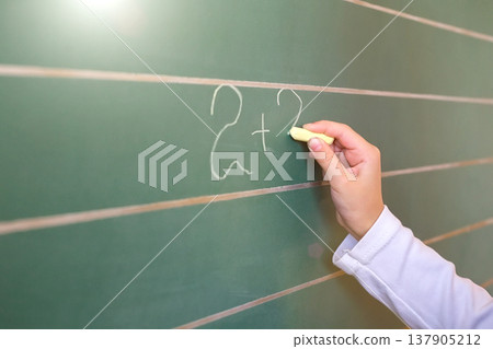 First grade pupil a girl writing on green blackboard at school lesson First grade pupil a girl writing on green blackboard at school lesson 137905212