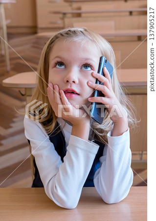 A first grade student at school speaks by phone. emotions of schoolgirls A first grade student at school speaks by phone. emotions of schoolgirls 137905217
