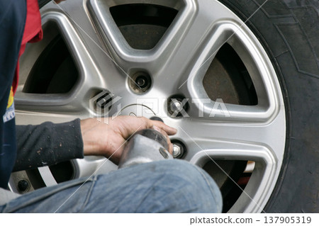 A mechanic using a tool to remove a car wheel. A mechanic using a tool to remove a car wheel. 137905319
