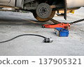 The side view shows the jack and tools used to lift the vehicle and remove the wheel. 137905321