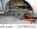 The side view shows the jack and tools used to lift the vehicle and remove the wheel. 137905322