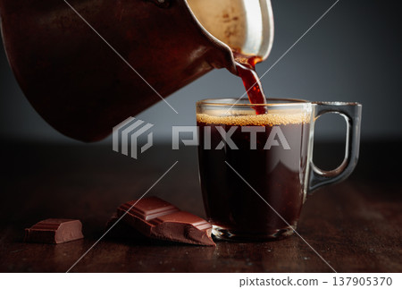 Black coffee is poured into a glass cup. Black coffee is poured into a glass cup. 137905370