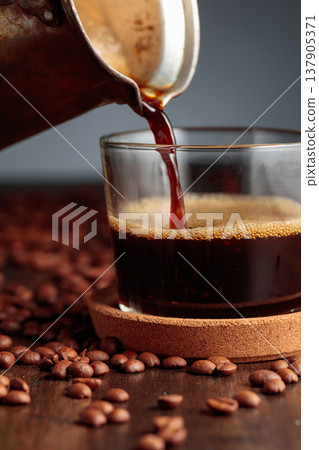 Black coffee is poured into a glass cup. Black coffee is poured into a glass cup. 137905371