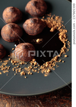 Chocolate truffles with cocoa powder and chocolate sauce on a black plate. Chocolate truffles with cocoa powder and chocolate sauce on a black plate. 137905399