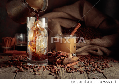 Black coffee is poured from a Turkish copper coffee pot into a glass with ice. Black coffee is poured from a Turkish copper coffee pot into a glass with ice. 137905411