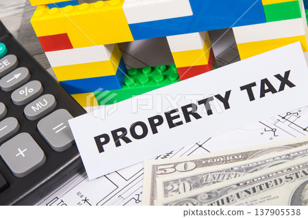 Inscription property tax with house made of toy blocks, dollar banknotes and calculator 137905538