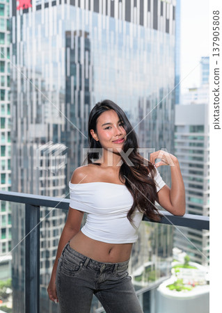 Young Asian woman posing on a high-rise balcony with modern skyscrapers in Kuala Lumpur, Malaysia 137905808