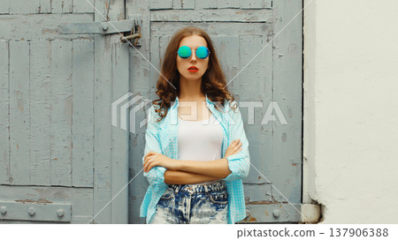 Portrait of stylish modern young woman in glasses, shorts posing on urban wall background Portrait of stylish modern young woman in glasses, shorts posing on urban wall background 137906388