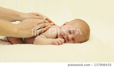 Mother gives massage to sleeping baby lying on the bed on white background, child and health concept Mother gives massage to sleeping baby lying on the bed on white background, child and health concept 137906410