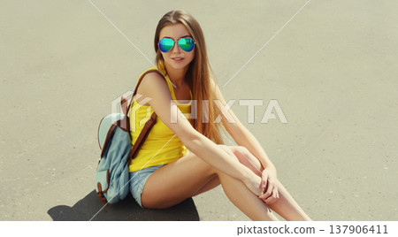 Stylish teenager girl with backpack, young woman sitting on city street on a summer day Stylish teenager girl with backpack, young woman sitting on city street on a summer day 137906411