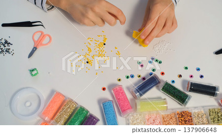 A girl creates a beaded dog figurine at her table while arranging small craft items in a cozy room 137906648