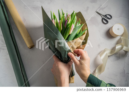Mother's day, birthday bouquet. Female hands wrapping tulip flowers in craft paper. Spring tulips flower background Mother's day, birthday bouquet. Female hands wrapping tulip flowers in craft paper. Spring tulips flower background 137906969