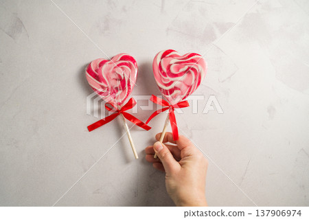 Valentine's Day festive background. Female hand holding heart-shaped lollipops on grey background with copy space. Love concept 137906974