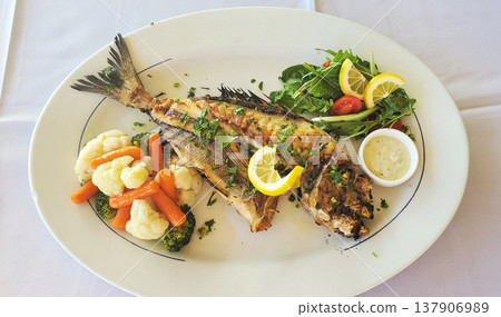 Fried dorado fish with vegetables, fresh lettuce, and lemon on a white plate Fried dorado fish with vegetables, fresh lettuce, and lemon on a white plate 137906989