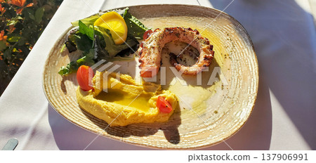 A fried octopus ring with a delicate puree, fresh lettuce leaves, a lemon wedge 137906991