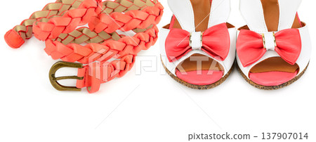 Trendy coral braided belt and white sandals with pink bows isolated on a white background. Fashionable summer accessories for women showcasing a vibrant and stylish seasonal look. Trendy coral braided belt and white sandals with pink bows isolated on a white background. Fashionable summer accessories for women showcasing a vibrant and stylish seasonal look. 137907014