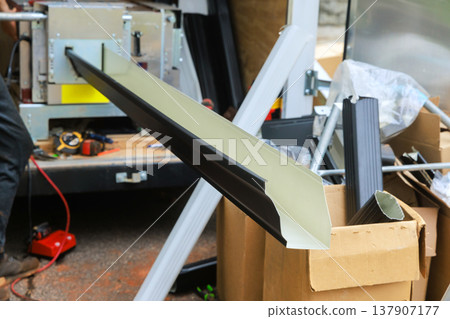 Worker using tools to fabrication aluminum gutter channels while materials organized nearby Worker using tools to fabrication aluminum gutter channels while materials organized nearby 137907177