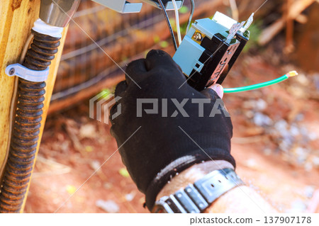 Worker connects electrical wires to control box in an outdoor setting 137907178