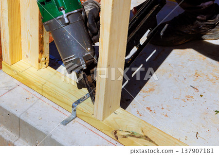 Worker uses pneumatic nail gun to secure wooden beams during construction at building site Worker uses pneumatic nail gun to secure wooden beams during construction at building site 137907181