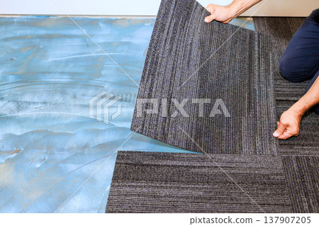Installing gray carpet tiles in modern room during home renovation Installing gray carpet tiles in modern room during home renovation 137907205